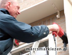 Marc van 't Veer staat op een trap en monteert een markies